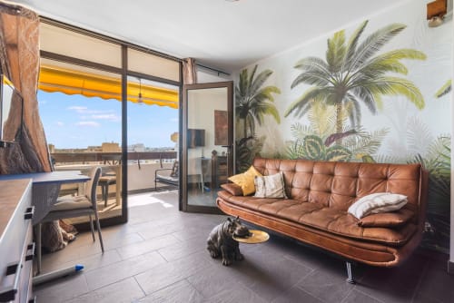 Moderno apartamento con sofá de cuero marrón, mural tropical y terraza con vistas al mar en Home Stay Gran Canaria