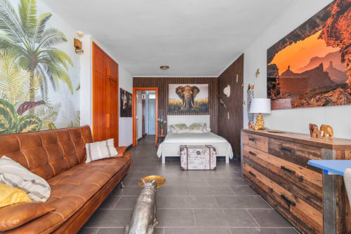 Estudio temático de safari africano con sofá de cuero coñac, cama blanca, cómoda de madera y arte de vida silvestre en Gran