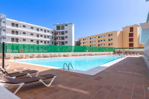 Piscina de Home Stay Gran Canaria con tumbonas, modernos edificios de apartamentos y cielo azul despejado en San Bartolomé de