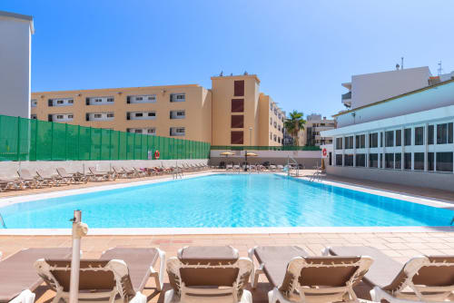 Piscina al aire libre con tumbonas en el complejo Home Stay Gran Canaria de San Bartolomé de Tirajana, rodeada de apartamentos