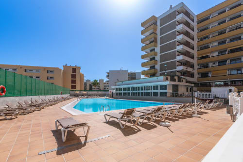 Soleada piscina del Home Stay Gran Canaria con tumbonas, piscina azul y edificios residenciales en San Bartolomé de Tirajana