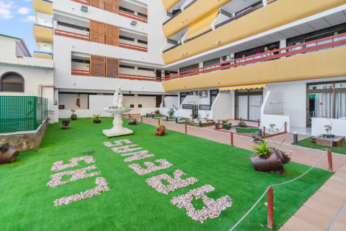 Patio con césped verde y letras de piedra blanca en Home Stay Gran Canaria, San Bartolomé de Tirajana, rodeado de