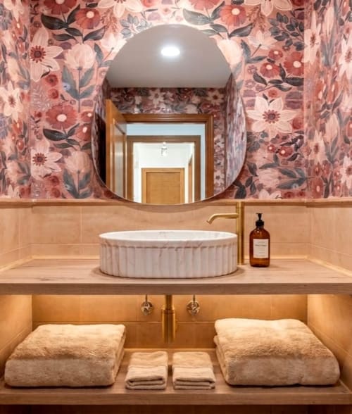 Baño moderno en Marbella Views con espejo redondo, lavamanos blanco, papel tapiz floral y toallas dobladas, Ojén España