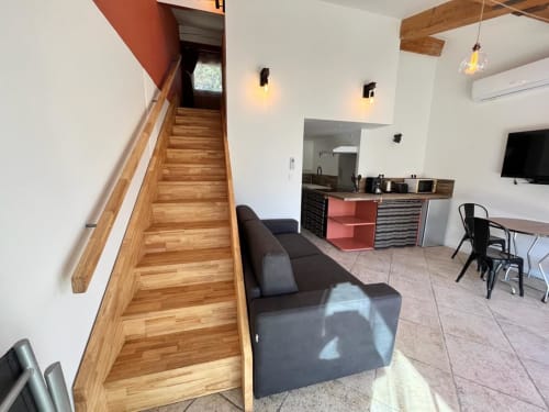 Espace de vie du gîte Romulus avec escalier en bois, canapé foncé, kitchenette et coin repas à Roumoules