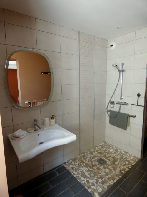 Modern bathroom at Les Rives De La Tronne with round mirror, white sink, and walk-in shower with pebble floor, Mer FR