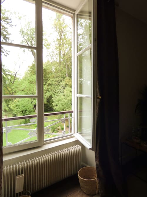 Open French doors revealing lush green forest views, radiator, and wicker basket in La Chambre Safran at Les Rives De La