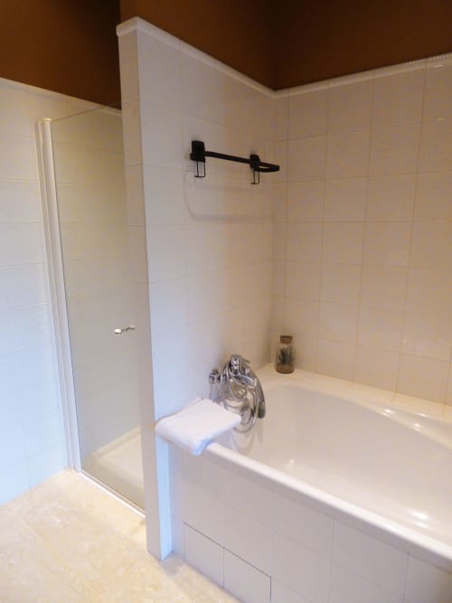 Modern bathroom with white tile walls, bathtub, glass shower enclosure, and black fixtures at Les Rives De La Tronne, Mer