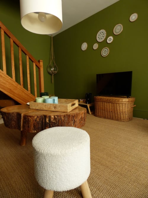 Modern living room with olive green walls, wooden stump coffee table, white poufs, and flat-screen TV at Les Rives De La