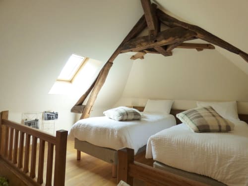 Bright attic bedroom with exposed wooden beams, two twin beds with striped pillows, skylight, wooden railings, at Les Rives
