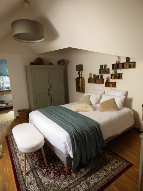 Bright bedroom with queen bed, cream bedding, gray throw, wooden floor, and wall shelving at Les Rives De La Tronne hotel in