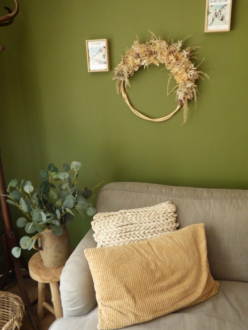 Cozy corner in La Suite de l'Orangerie with sage green walls, dried flower wreath, beige armchair with cushions, and fresh