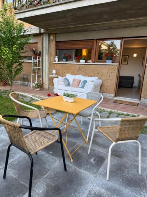 Terrazza all'aperto di Il Giardinetto di Elelú a Orvieto con tavolo giallo, sedie in vimini e divano bianco visibili attraverso il vetro