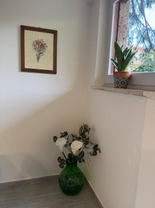 Angolo luminoso della camera B&B a Orvieto con fiori bianchi in vaso verde, arte botanica incorniciata, pianta in vaso sul davanzale