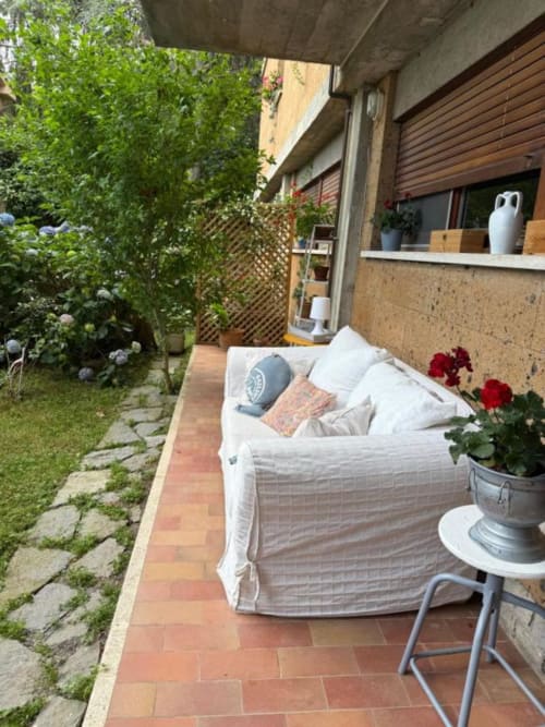 Accogliente spazio esterno a Il Giardinetto di Elelú a Orvieto con divano bianco, fiori rossi e vista sul lussureggiante giardino