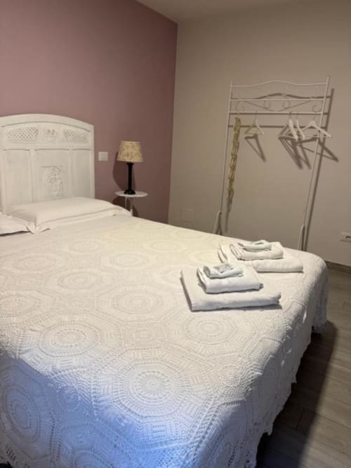 Camera luminosa in B&B a Orvieto con letto bianco, asciugamani piegati, parete accent rosa, lampada da comodino e appendiabiti in metallo