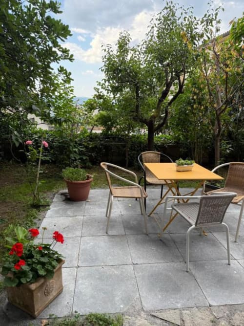 Patio del giardino di Il Giardinetto a Orvieto con tavolo da pranzo all'aperto, sedie in vimini, piante fiorite e alberi con vista mare