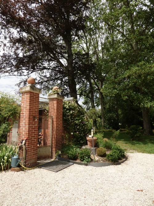 Entrée de la gatehouse historique en brique rouge à Les Rives De La Tronne à Mer, France, entourée de jardins luxuriants et de grands arbres