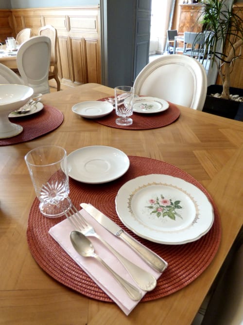 Elegant dining table setting at Les Rives De La Tronne with floral plates, burgundy placemats, and formal place settings.