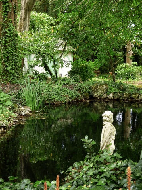 Stone bust statue beside tranquil pond at Les Rives De La Tronne garden in Mer, France
