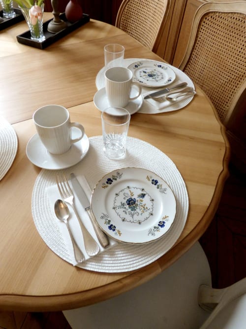 Mise en place élégante aux Rives De La Tronne avec assiettes décorées, tasses blanches, couverts et verres sur table en bois