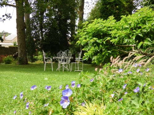 Ornate white garden furniture set on manicured lawn surrounded by purple flowers and lush greenery at Les Rives De La Tronne,