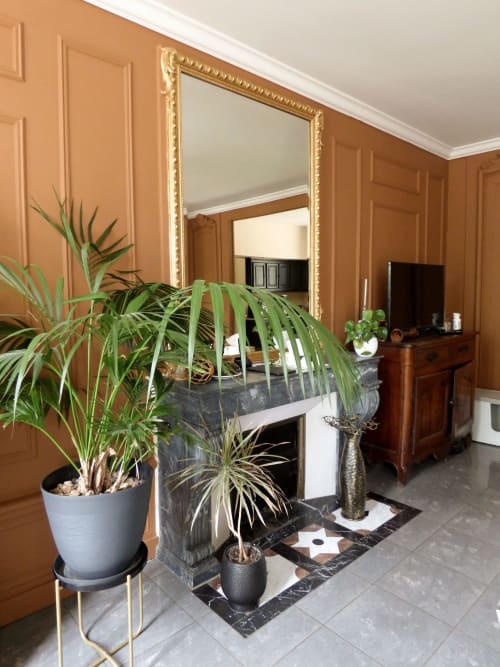 Elegant foyer at Les Rives De La Tronne with terracotta walls, ornate gold mirror, potted palms, and black marble fireplace.