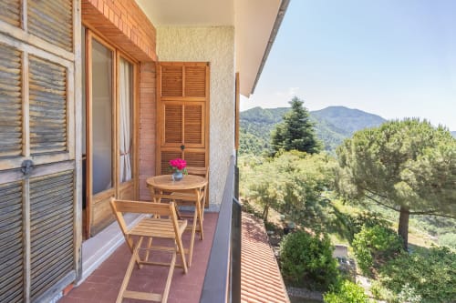 Balcon de la Chambre Gioia à l'hôtel Allegria à Bajardo avec vue sur les montagnes, mobilier en bois et fleurs roses