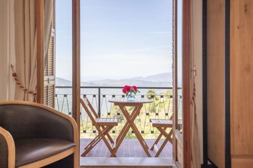 Chambre de l'hôtel Alegria à Bajardo s'ouvrant sur un balcon avec vue sur le lac de montagne et mobilier en bois