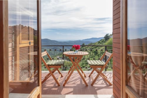 Balcon de l'hôtel Allegria à Bajardo avec vue sur les montagnes, table et chaises en bois avec fleurs roses