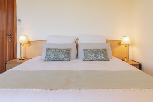 Lit double élégant à la Chambre Gioia de l'hôtel Allegria, Bajardo, avec draps blancs, coussins patterisés et lampes de chevet