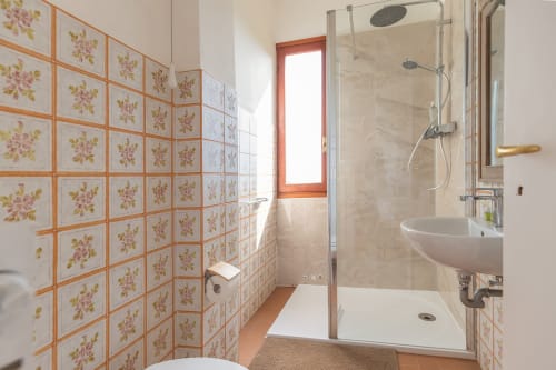 Salle de bains avec carrelage fleuri vintage, douche vitrée, lavabo blanc et fenêtre à l'hôtel Allegria de Bajardo, Italie