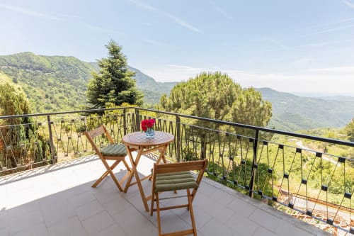 Balcon de l'hôtel Allegria à Bajardo avec vue montagne, chaises en bois et table fleurie