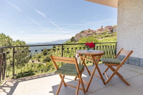 Balcon de l'hôtel Allegria à Bajardo avec chaises en bois, table, fleurs rouges et vue sur la vallée montagne