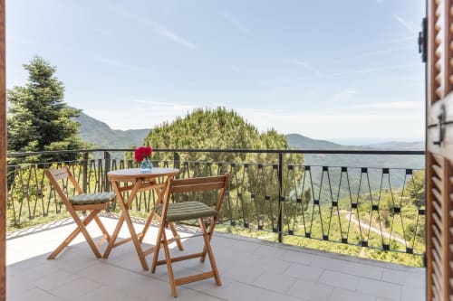 Chaises en bois autour d'une table sur la terrasse de l'hôtel Allegria à Bajardo, vue panoramique sur les montagnes et les cyprès
