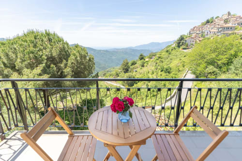 Vue du balcon de l'hôtel Allegria à Bajardo avec paysage montagneux, chaises en bois et fleurs rouges