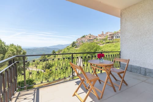 Balcon de la Chambre Infinito à l'hôtel Allegria à Bajardo avec vue sur les montagnes, chaises en bois et village perché en arrière-plan