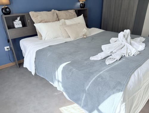 Suite moderne à Au Richebourg Nogent avec mur accent bleu, lit gris, serviettes blanches et table de nuit intégrée