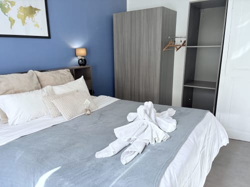 Chambre moderne aux murs bleus à l'hôtel Au Richebourg Nogent, avec lit gris, serviettes décoratives en forme d'animaux et décor de mappemonde