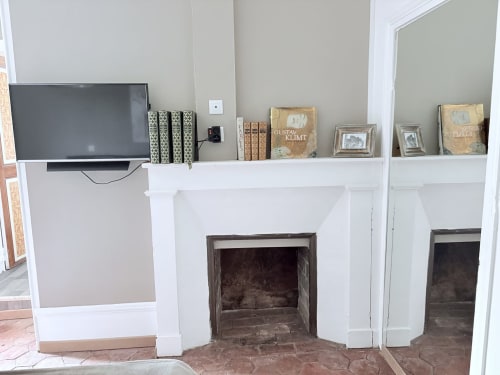 Cheminée moderne à manteau blanc dans la Suite Paul Dubois du gîte Au Richebourg Nogent, avec télévision, livres et photos encadrées