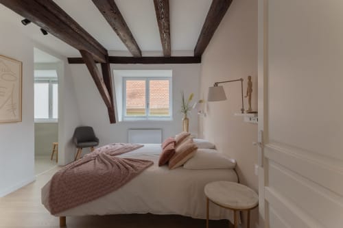 Cozy duplex bedroom in Colmar with exposed beams, cream bedding, and rustic wooden accents