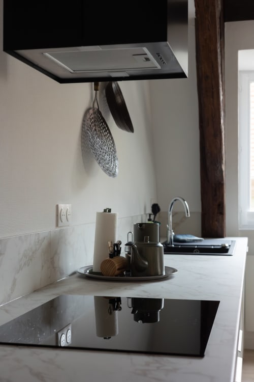 Modern kitchen countertop with black stovetop, marble surface, white backtile, range hood, and kitchenware at Le JO·LIE