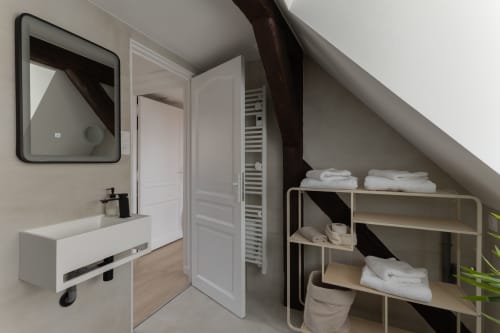 Modern bathroom and storage area in Le JO·LIE Duplex, Colmar, featuring sink, mirror, and shelving with towels