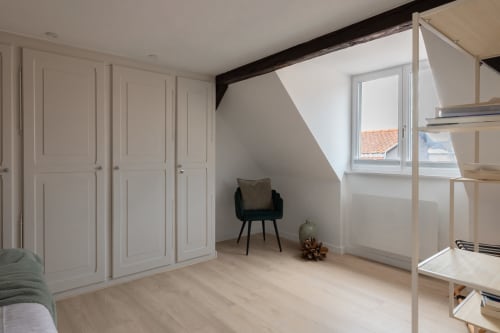 Modern attic bedroom at Le JO·LIE Duplex in Colmar with white built-in wardrobes, wooden shelving, and bright skylight window