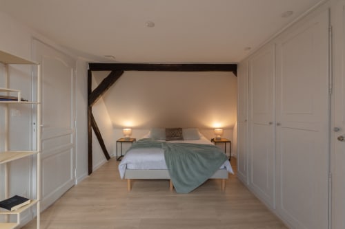 Spacious attic bedroom at Le JO·LIE Duplex, Colmar with exposed beams, bed, nightstands, and ambient lighting