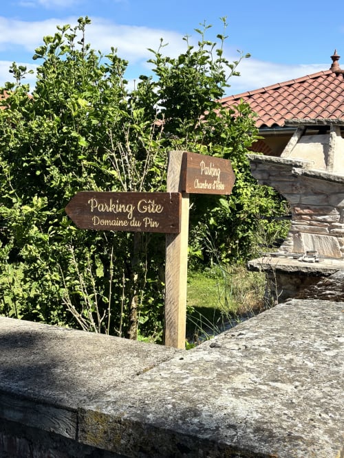 Panneaux directionnels en bois au gîte Le Domaine du Pin à Romans, France, entourés de végétation verte