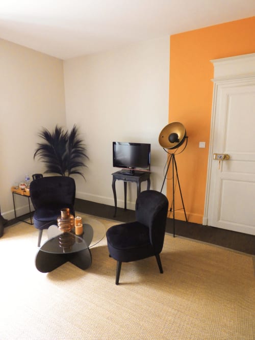 La Chambre Safran at Les Rives De La Tronne features modern black furniture, a flat-screen TV, and vibrant orange accent wall