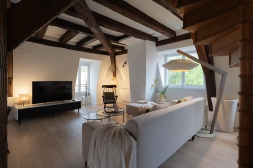 Spacious duplex living room in Colmar with exposed wooden beams, white sofa, TV, and large windows