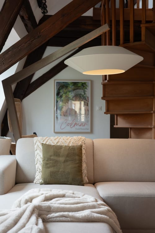 Cozy Colmar loft with exposed beams, modern pendant light, cream sofa, and green pillow