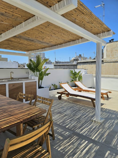Rooftop terrace at Pura Vita Apartments in Monopoli with wooden pergola, lounge chairs, dining area, and city views