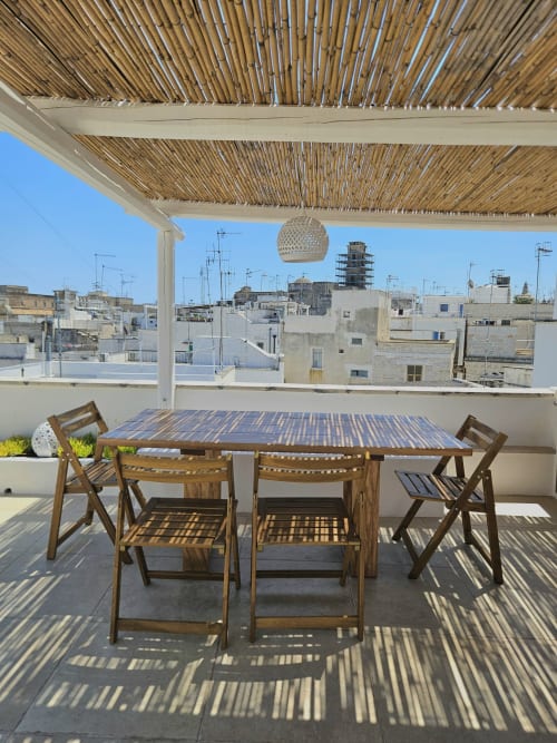 Sunny rooftop terrace at Pura Vita Apartments in Monopoli with wooden dining furniture and pergola shade overlooking historic
